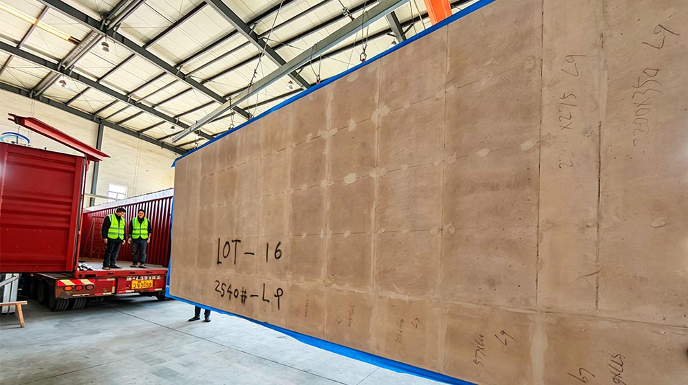 Large prefabricated wall panel in a warehouse with construction workers inspecting it, part of the DEEPBLUE SMARTHOUSE panelized system.