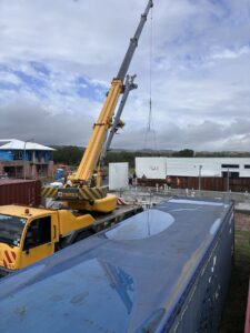 A large yellow crane is lifting a white container at the Deepblue construction site under a cloudy sky.