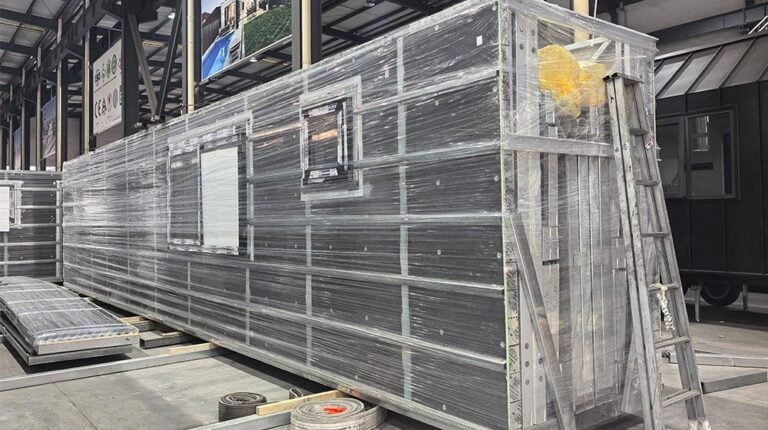 Een grote modulaire containerconstructie van metaal en glas, voorzien van een ladder, staat buiten op een industrieterrein.