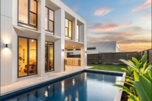 Contemporary house with large glass windows and a swimming pool in the backyard during sunset, showcasing modern architecture and outdoor living space.