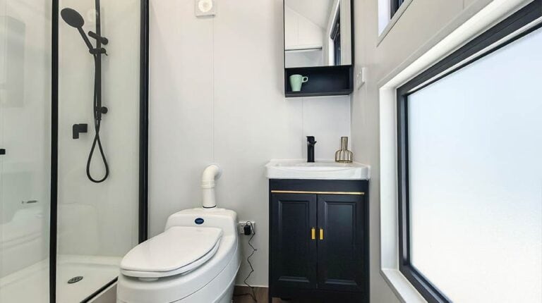 Contemporary bathroom featuring a glass shower enclosure, a sleek toilet, and a dark vanity with a mirror, illuminated by natural light from large windows.