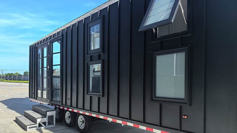 Contemporary black mobile office container with multiple windows and a door, set outdoors on a sunny day, ideal for remote work or temporary office space.