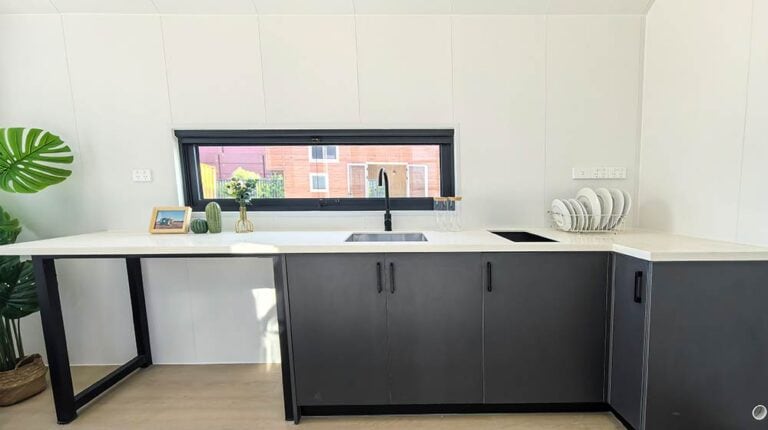 Contemporary kitchen featuring black lower cabinets, white countertop, and a large window with a view of neighboring buildings.