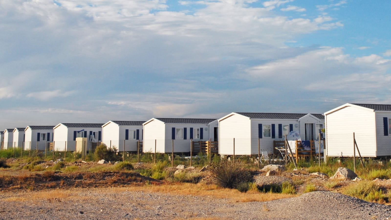 A row of white prefab social housing units with modular design, set in an open landscape under a partly cloudy sky, showcasing affordable and quick-to-construct housing solutions.