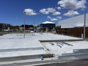Construction site with metal framework and concrete foundation at Deepblue, under a blue sky with clouds, showing ongoing building development.