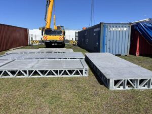 Construction site with metal platforms, shipping containers, and a crane in the background, under a clear blue sky.