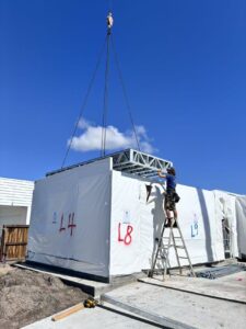 Worker installing a large modular building with a crane, focusing on the structural framework and construction process.