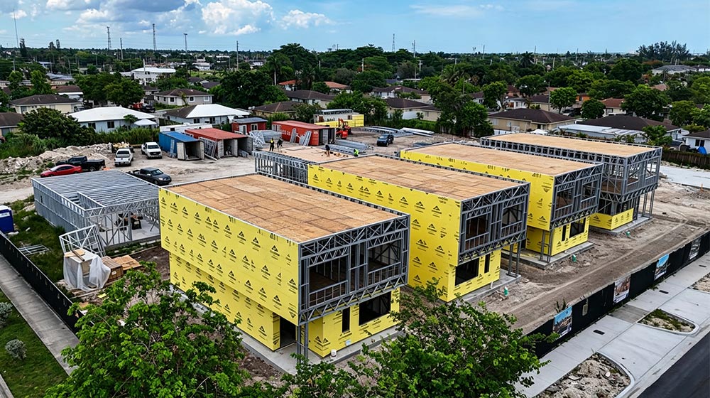 Aerial view of new residential buildings under construction with yellow sheathing in a suburban area, showing progress in development.