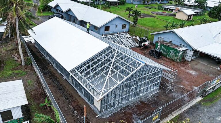 Construction site of a steel frame villa with a white roof, surrounded by greenery and other similar structures, showcasing modern prefab building techniques.