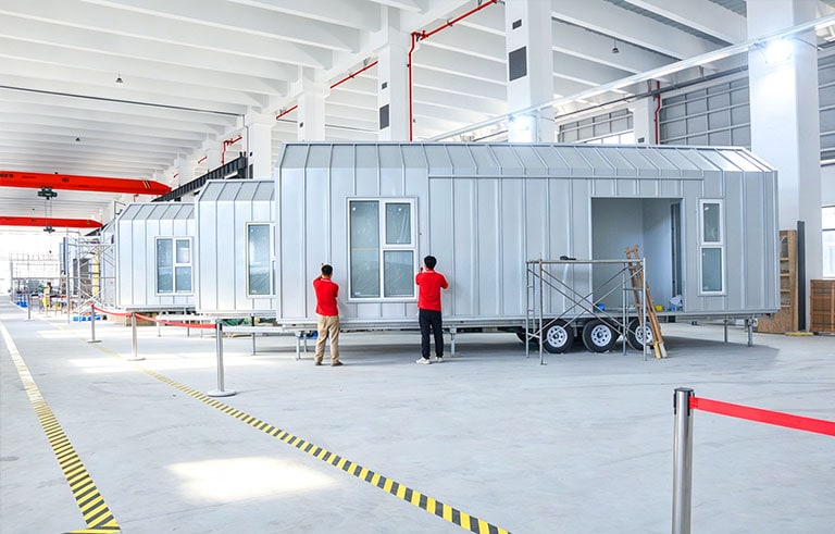 Two workers inspecting modern modular prefabricated homes inside a spacious industrial warehouse.