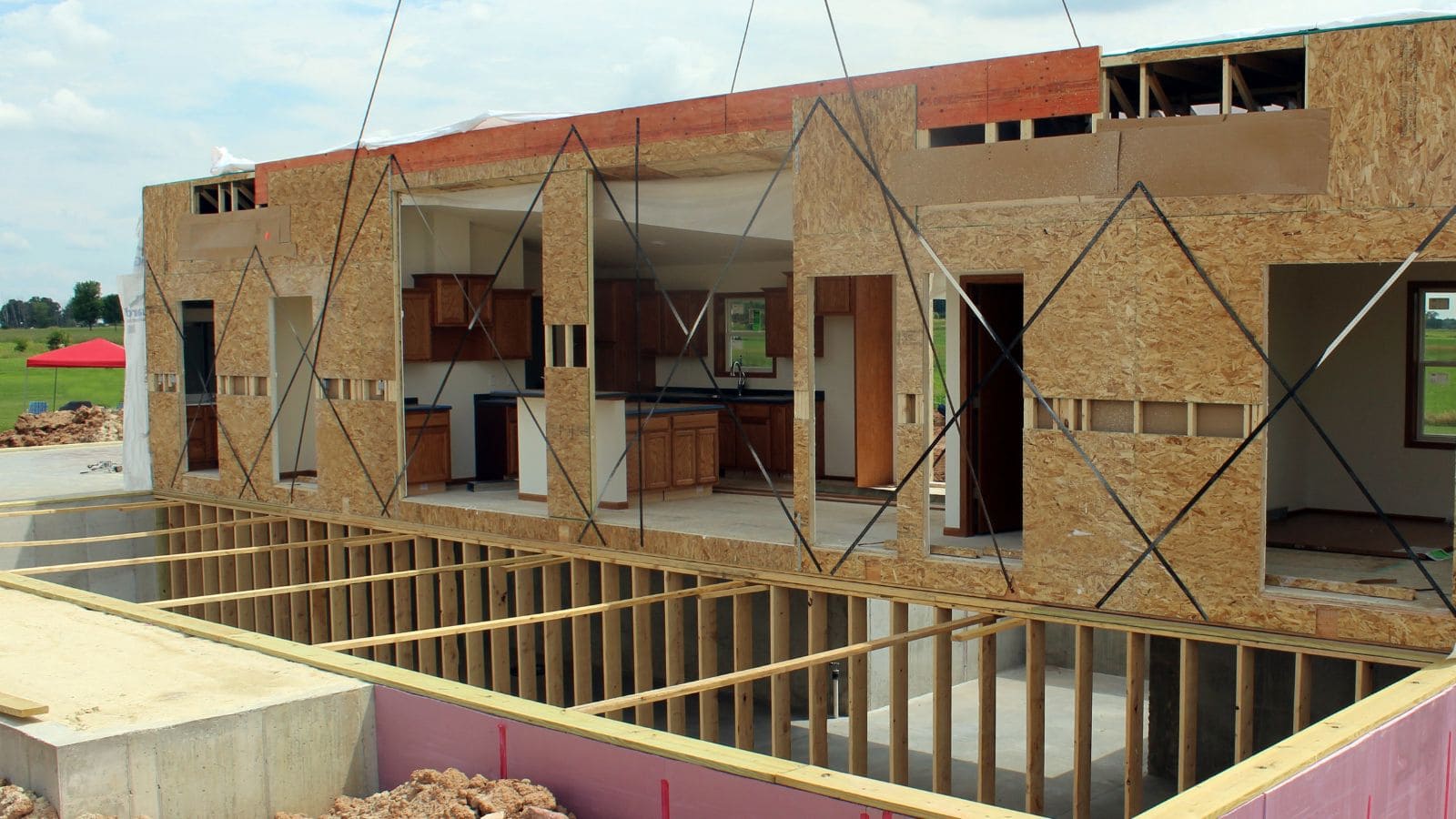 Construction site of a prefab home showing wooden framing and partial exterior walls, with open spaces for windows and doors, under a clear sky.
