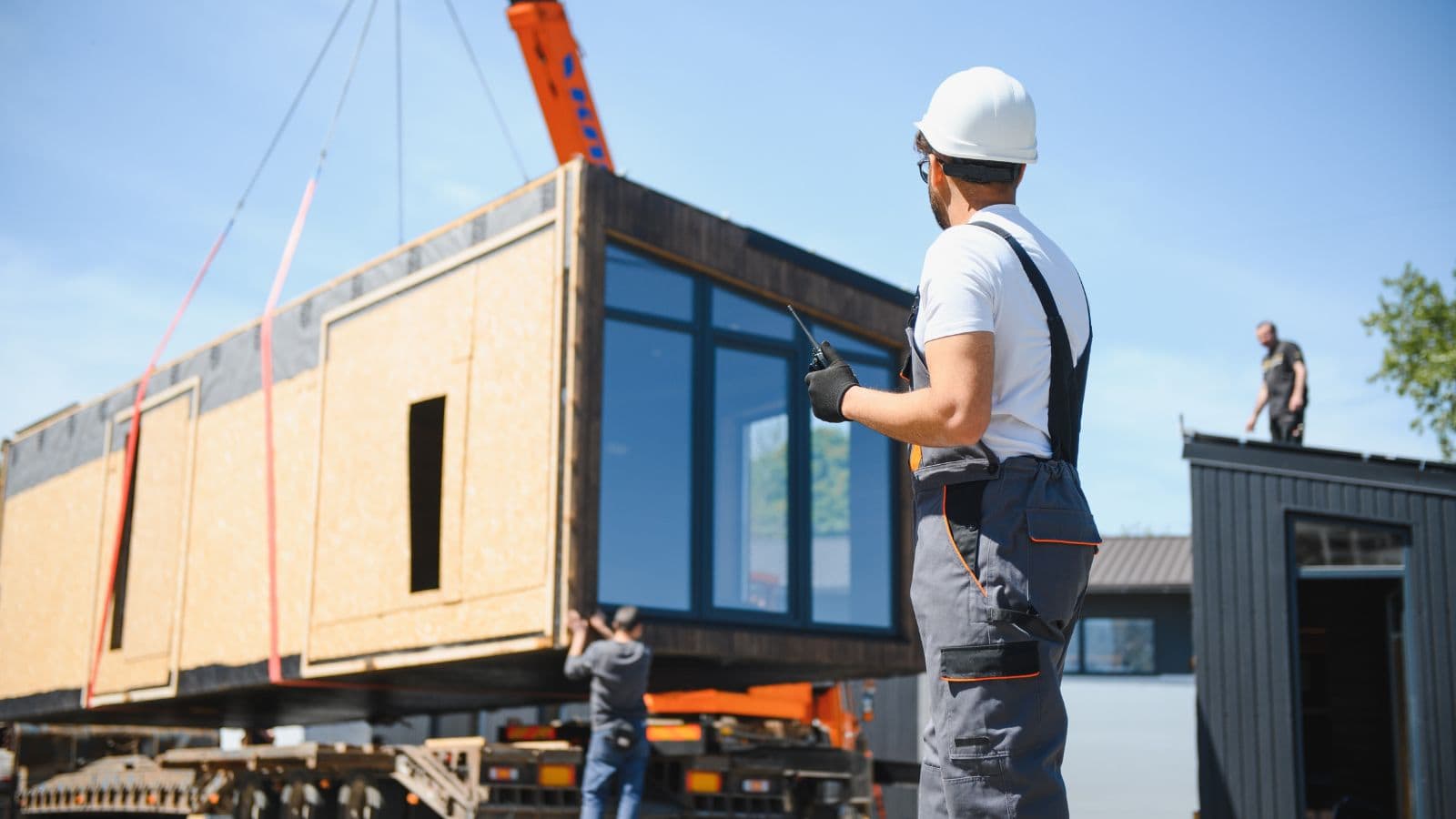 Construction worker overseeing the installation of prefabricated modular building sections with crane support, emphasizing offsite manufacturing benefits.