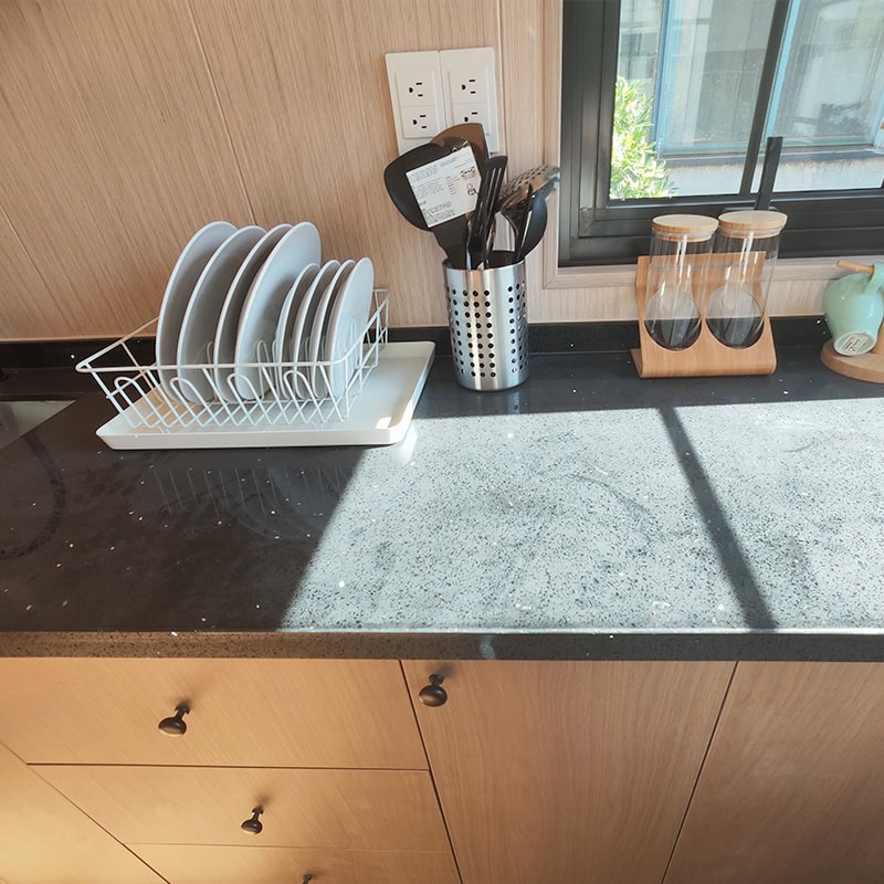 Kitchen countertop with dish rack, utensils, and glass jars near window, showcasing a clean and organized space in a tiny house.
