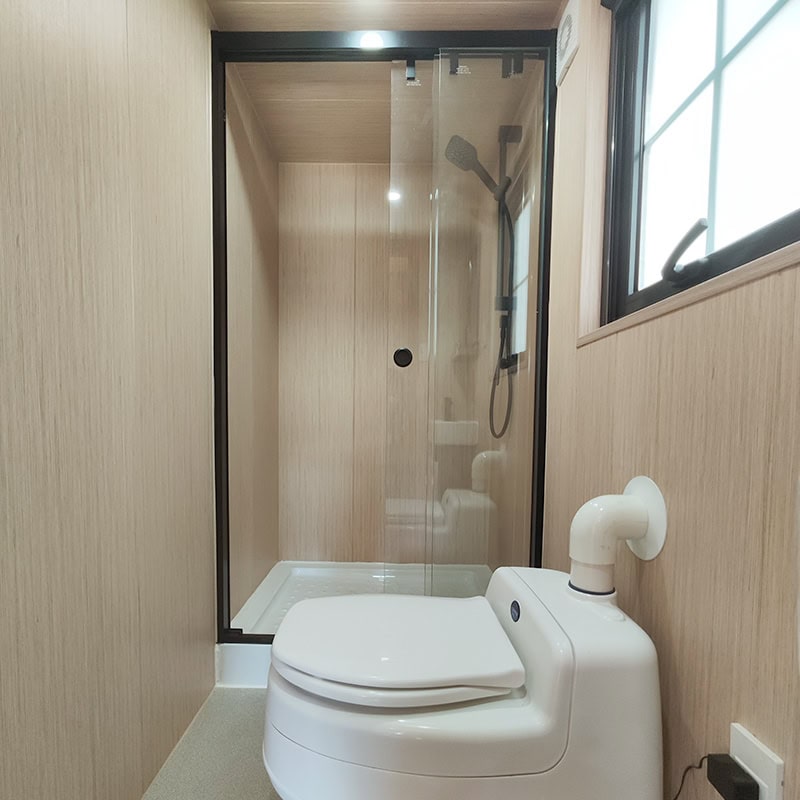 Interior view of a compact tiny house bathroom featuring a modern shower enclosure and a high-tech toilet.