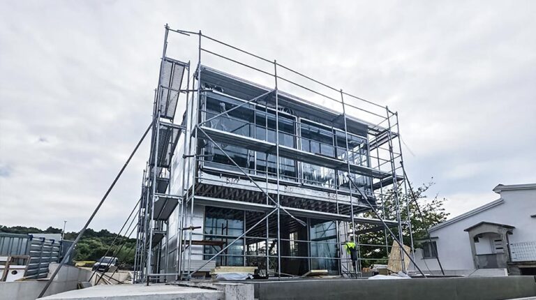 Construction site showing a modern multi-story building with scaffolding and workers installing windows.