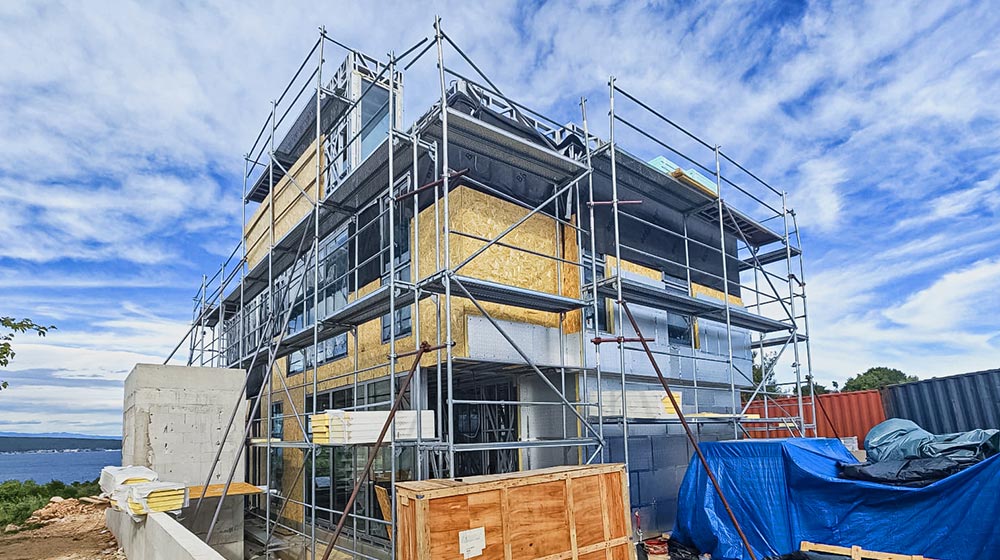 Construction site of a modern building with scaffolding, blue sky, and clouds, showing ongoing development and structural work.