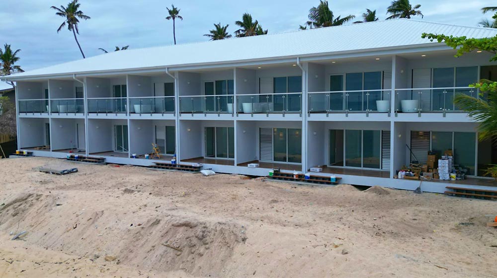Modern pre-fab hotel with light steel frame and two-story design on a tropical beach in Fiji, featuring spacious balconies and large glass windows.
